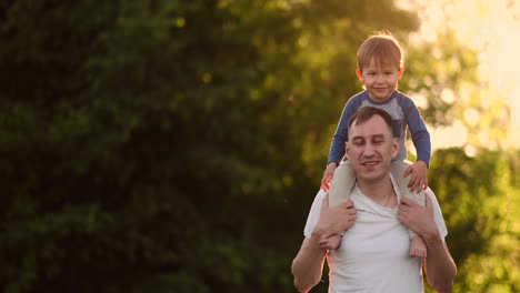 padre amoroso sonríe caminando con el niño sentado en el cuello al atardecer en un prado en verano en cámara lenta.