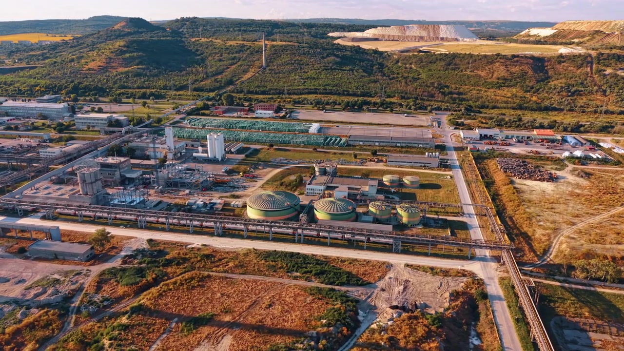 Industrial facility with storage tanks. An aerial view reveals large green cylindrical reservoirs and extensive piping systems near green hills.