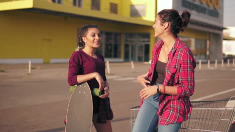 two hipster girls standing by the shopping cart on parking by the citymall during sunset