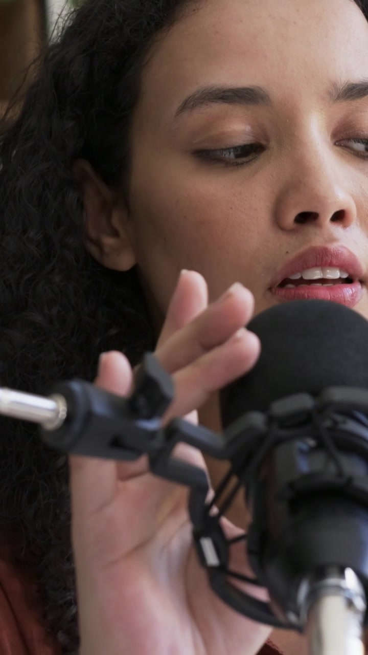 Video verticale: Podcaster che si prepara a registrare con un top color ruggine, mentre regola il filtro anti-pop del microfono nel suo studio casalingo