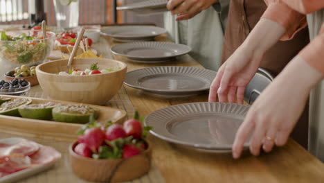 the hands of three women setting the table for a gathering of friends