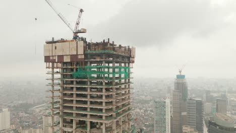 Aerial-tilting-pedestal-view-of-tall-skyscraper-under-construction-in-urban-city-center-on-a-cloudy-day