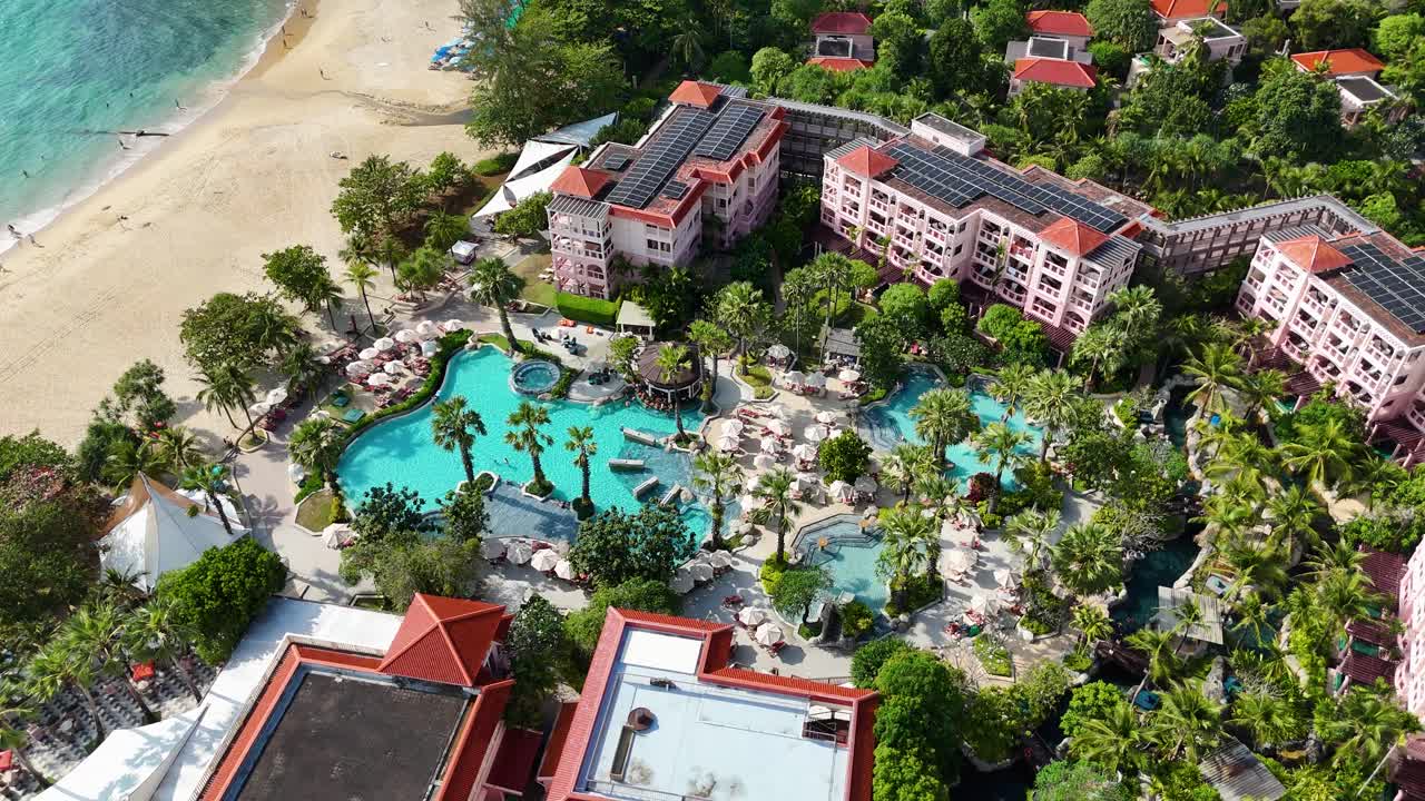 Aerial footage of a luxury resort in Phuket, Thailand, showcasing pools, lush greenery, and beachfront under bright daylight