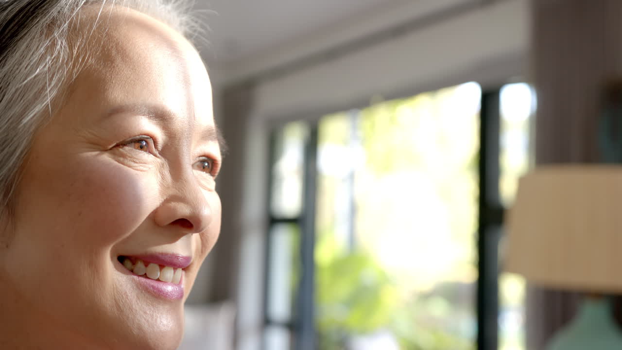 Smiling senior asian woman looking outside window, enjoying peaceful moment at home