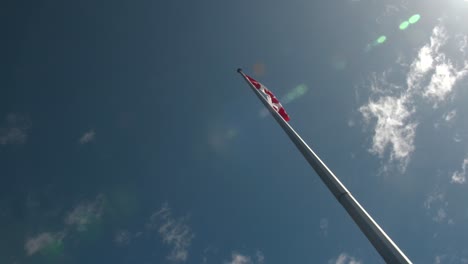 lens flair over canadian flag waving atop flagpole.slider