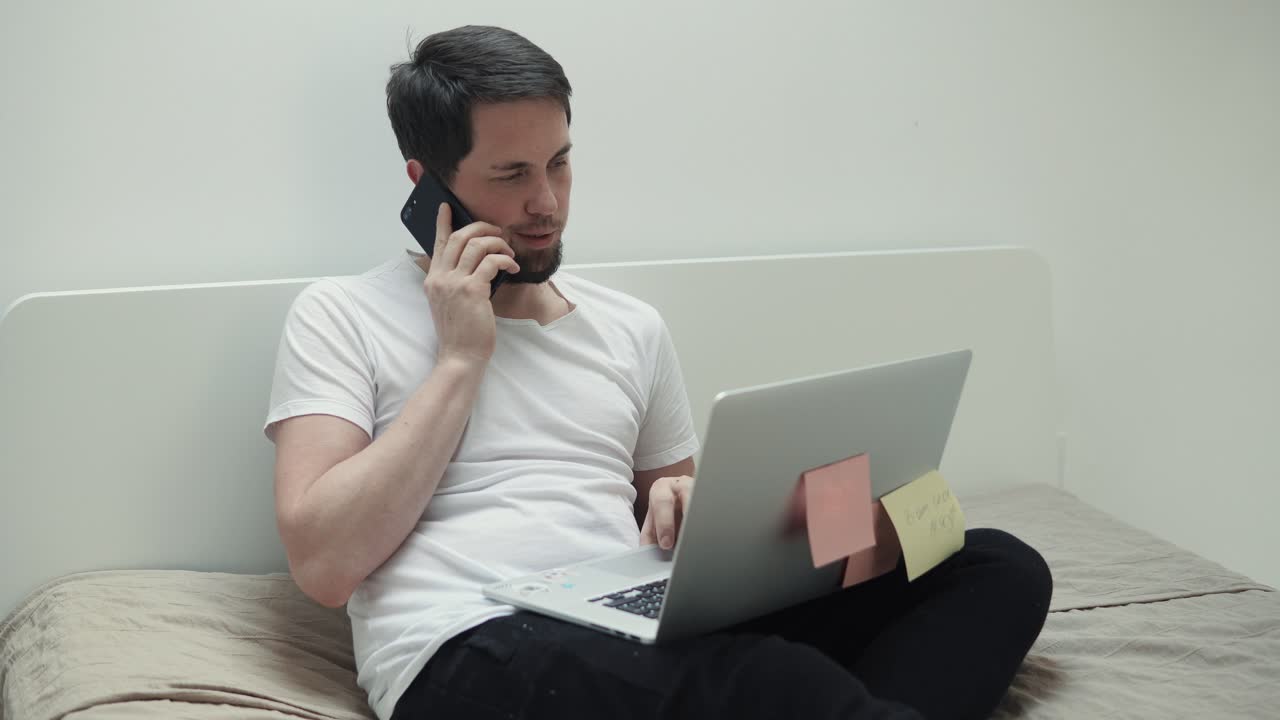 침대에서 노트북과 전화로 일하는 남자