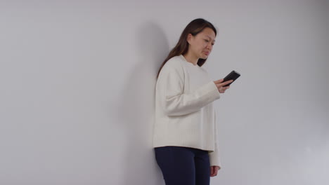 stressed or anxious woman sitting on floor leaning against wall at home reacting to internet or social media news message or story on mobile phone 8