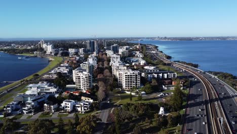 Vista-Aérea-De-Drones-De-La-Autopista-Que-Viaja-Por-La-Península-De-South-Perth-Con-Edificios-De-Apartamentos-Y-La-Costa-Con-El-Río-Swan