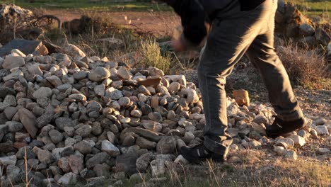 young man living in the countryside picks up stones outdoors under the golden light of the afternoon