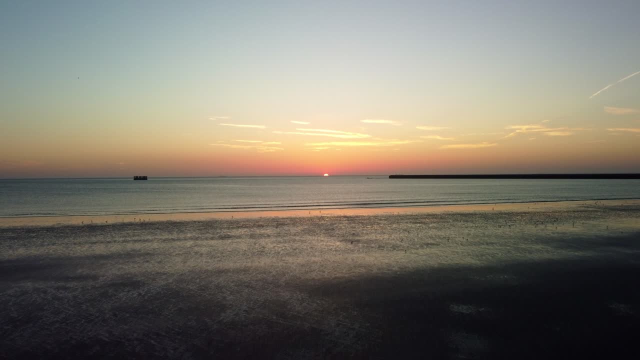 Drone video heading out to sea of the coast of Hunstanton, Norfolk as the sun sets over the ocean horizon.