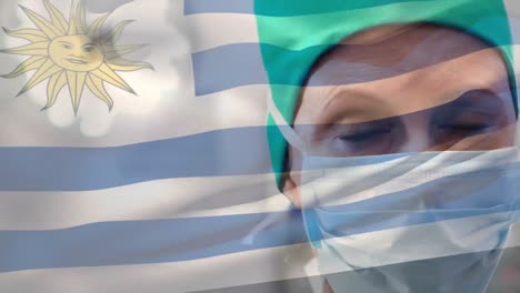 Animation-of-waving-uruguay-flag-against-caucasian-female-surgeon-in-surgical-mask-at-hospital