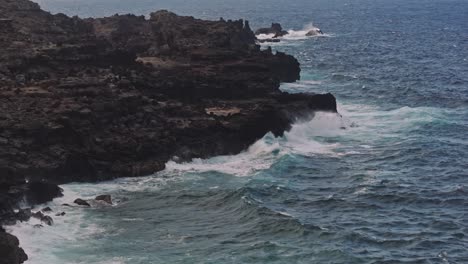 Aerial-slow-panning-shot-of-jagged-rocks-along-the-coast-with-waves-crashing-against-them