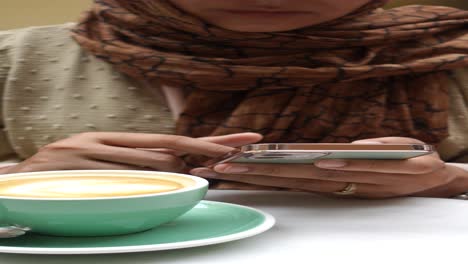 woman in hijab sitting at a coffee shop using her phone