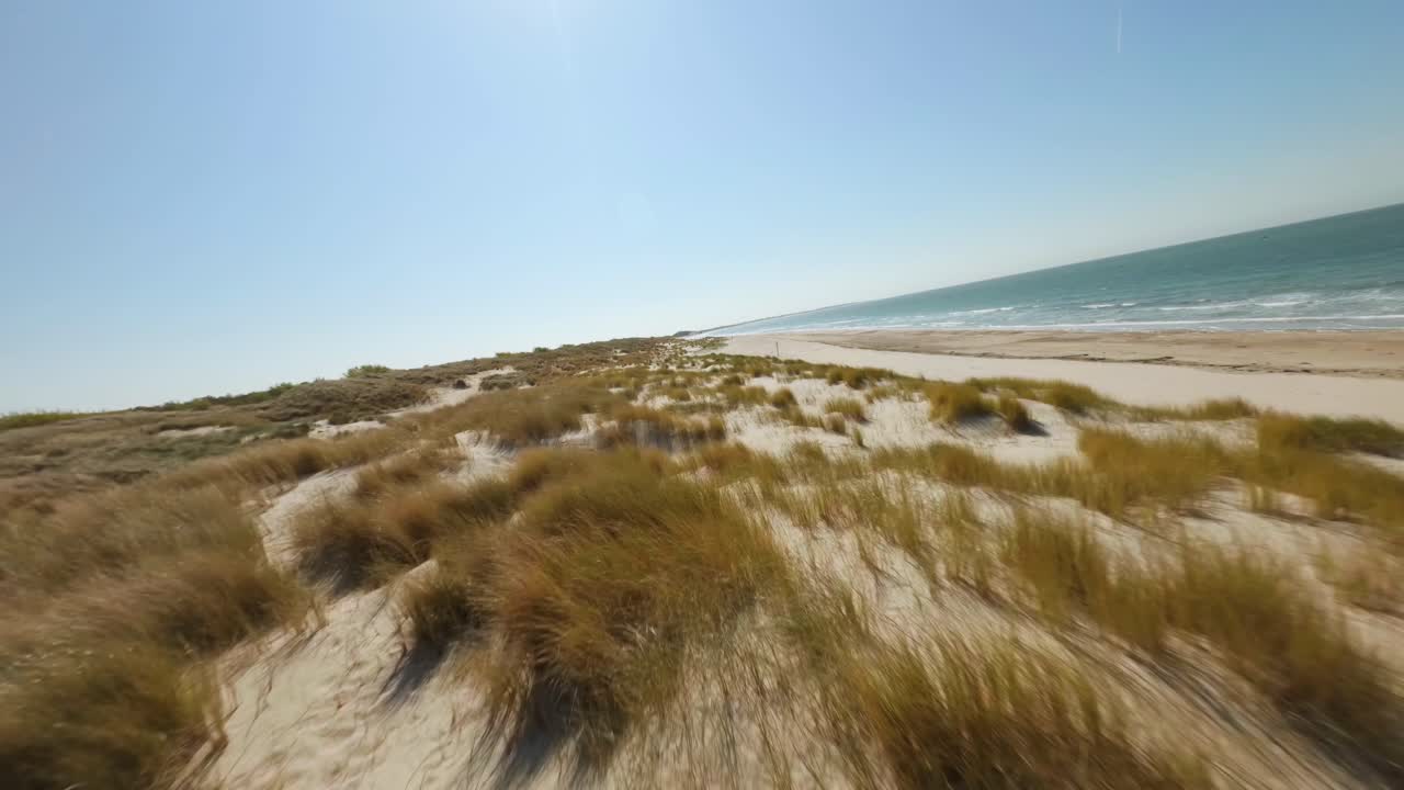 Close-up opname van de ontmoetingsplek van de golvende, azuurblauwe zee en de zanderige, met gras begroeide kustlijn