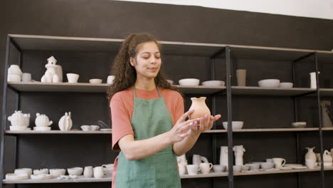 smiling female clerk holding a clay jug and taking photo in the pottery shop