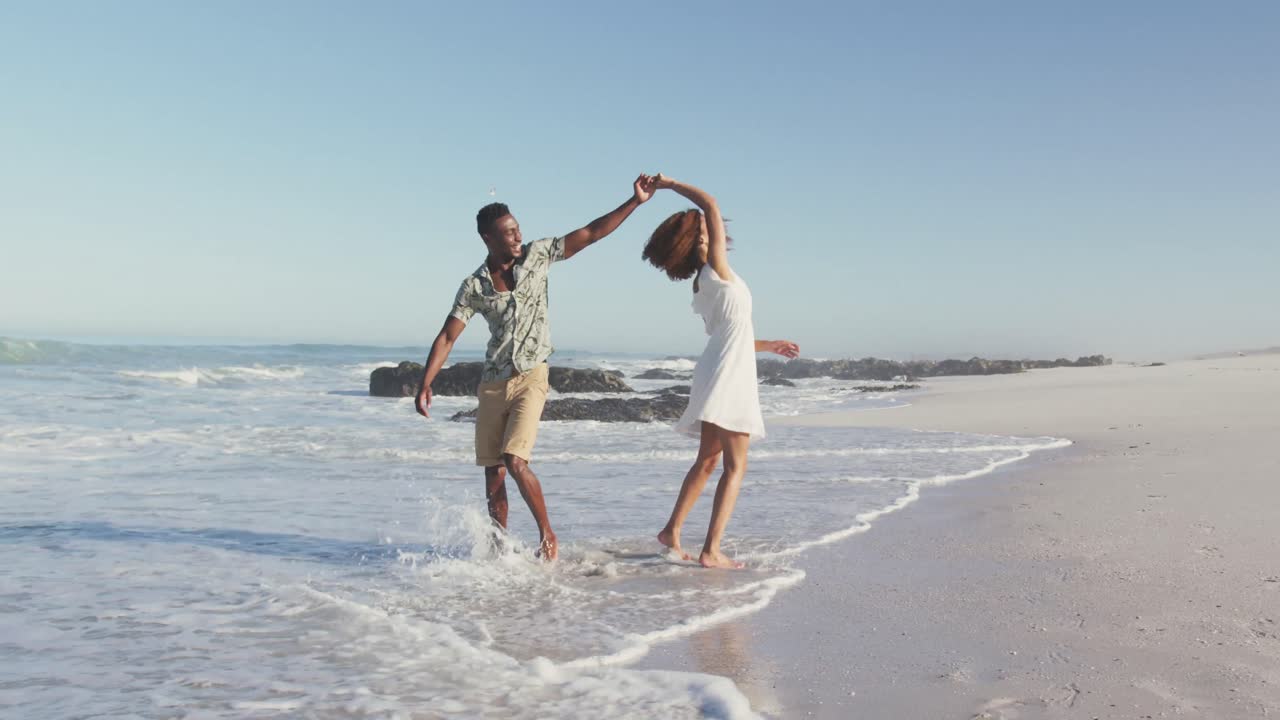 pareja afroamericana caminando por la playa y besándose