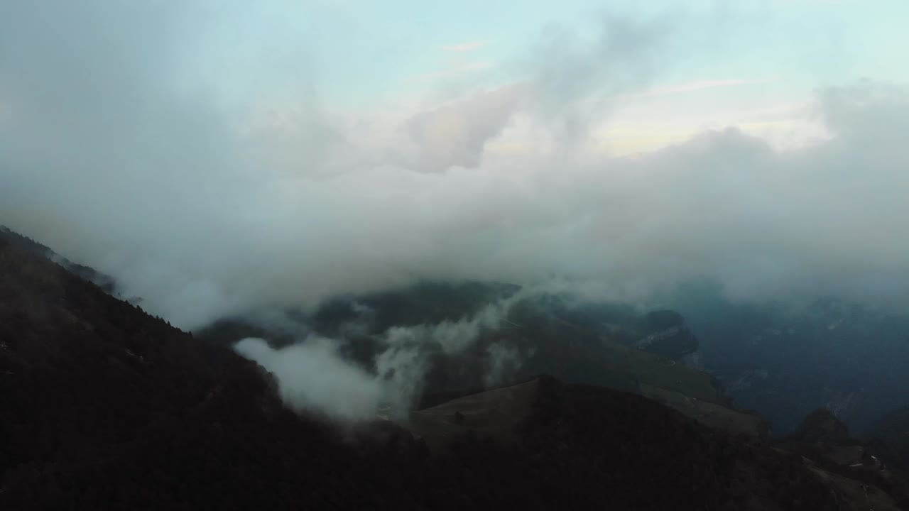 Aerial drone view of Himalayan foothills covered in thick mist and low clouds with mountain silhouettes fading into distance creating dramatic and mysterious natural scenery during evening light