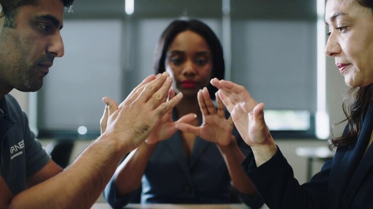 Reacting to cue, two colleagues in business attire moving hands inward at table, woman mirroring
