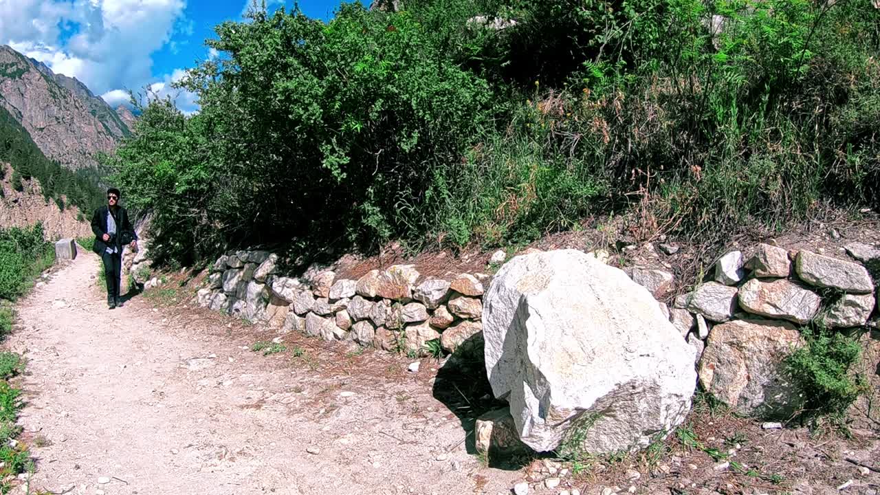 fotógrafo de la naturaleza caminando por el sendero con una enorme roca en un día soleado - toma amplia