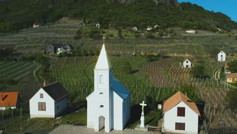 Afternoon-upward-movement-drone-view-above-the-countyside-fields-with-little-church-and-cross