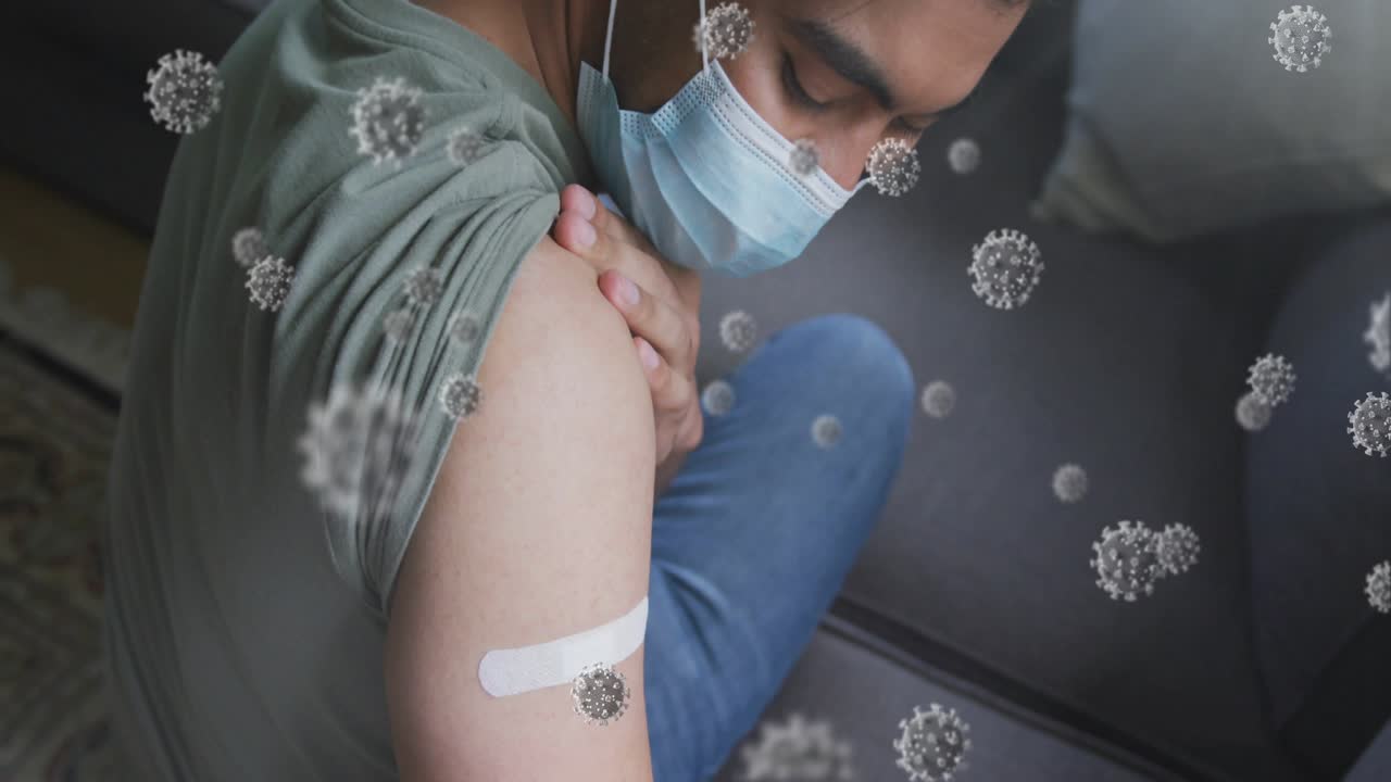 Uomo seduto sul divano che alza la manica e controlla la fasciatura mentre elementi grafici del virus si sovrappongono alla salute