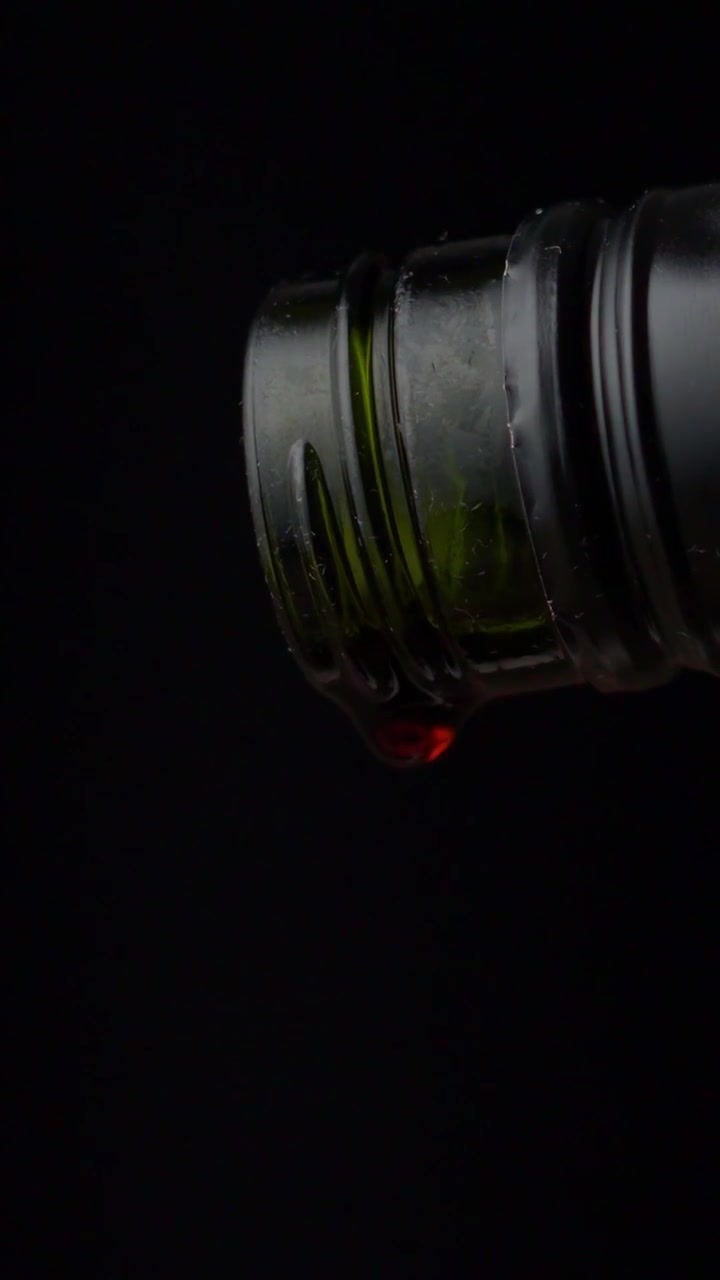 Vino tinto goteando de una botella sobre fondo negro, vertical, a cámara lenta, 50 fps