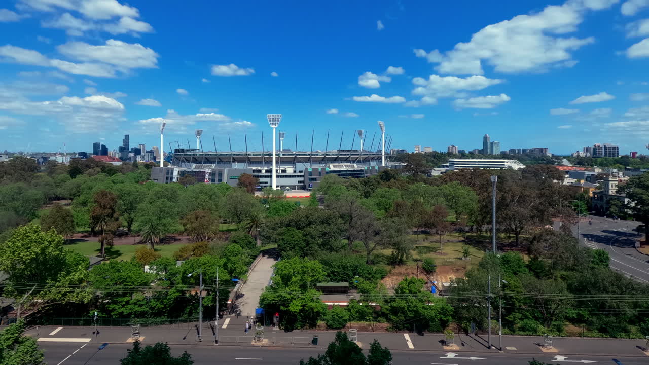 Tidsforløb af Melbourne Cricket Ground (MCG) set fra Pullman on the Park med udsigt over Yarra Park i Melbourne, Australien, med byens skyline og skiftende lys over stadionet.