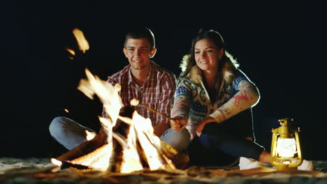 Man-And-Woman-Relaxing-Evening-Around-The-Campfire-Roast-Marshmallows-On-Sticks-Fire