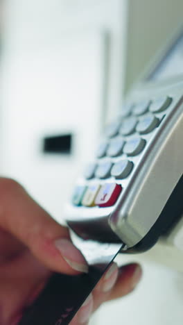 dama con camisa rosada, corto y cadena de muñeca inserta tarjeta negra en la máquina atm blanca para completar la transacción de pago mientras presiona el botón, fondo borroso con artículos poco claros
