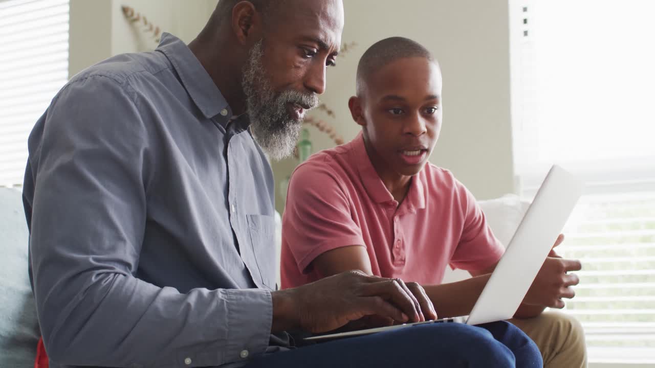 Video of happy african american father and son using laptop together