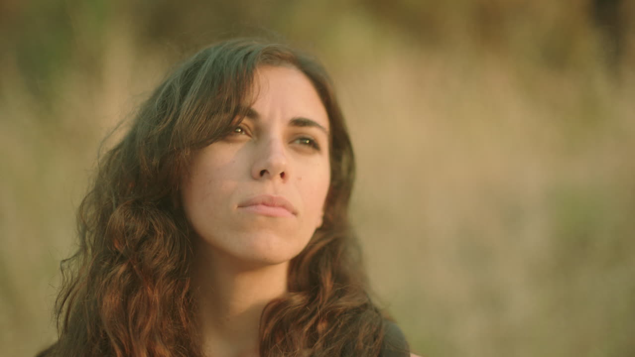 retrato de una atractiva mujer joven de etnia caucásica de fondo al aire libre, mirando más allá de la cámara y sonriendo a la cámara