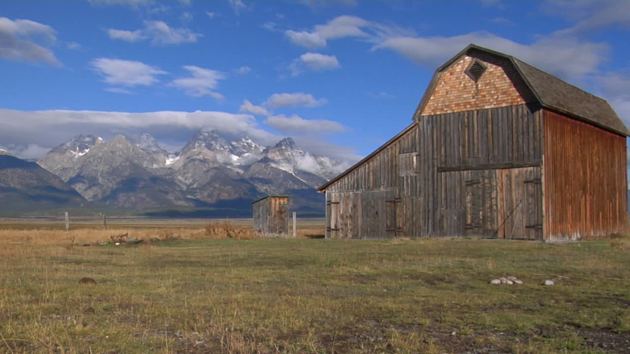 un viejo granero se eleva en una pradera con los grand tetons al fondo 9