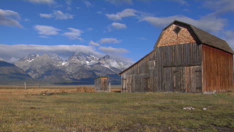 un viejo granero se eleva en una pradera con los grand tetons al fondo 9