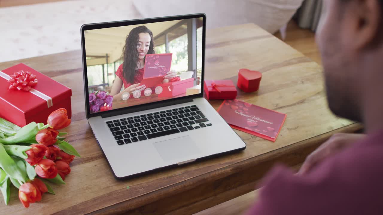 Happy biracial woman with vitiligo reading valentine card on valentine's day video call on laptop