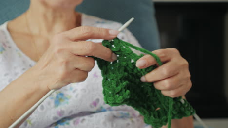 elderly woman knitting a green garment