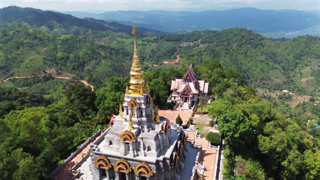 aerial wide pullback of wat santikhiri hilltop temple surrounded by thick trees and forested slope, mae salong, chiang rai thailand