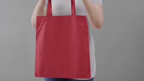 mujer caucásica con camiseta blanca sosteniendo una bolsa roja sobre un fondo gris, espacio de copia, cámara lenta