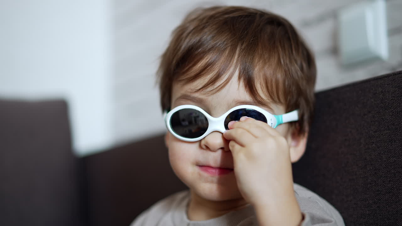 Face of a cute Caucasian baby boy putting on the sunglasses. Portrait of an adorable toddler close up.