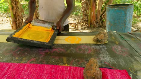 Afrikanischer-Mann-Druckt-Ethnische-Symbole-Mit-Farbe-Auf-Traditionelle-Kente-gelbe-Stoffe