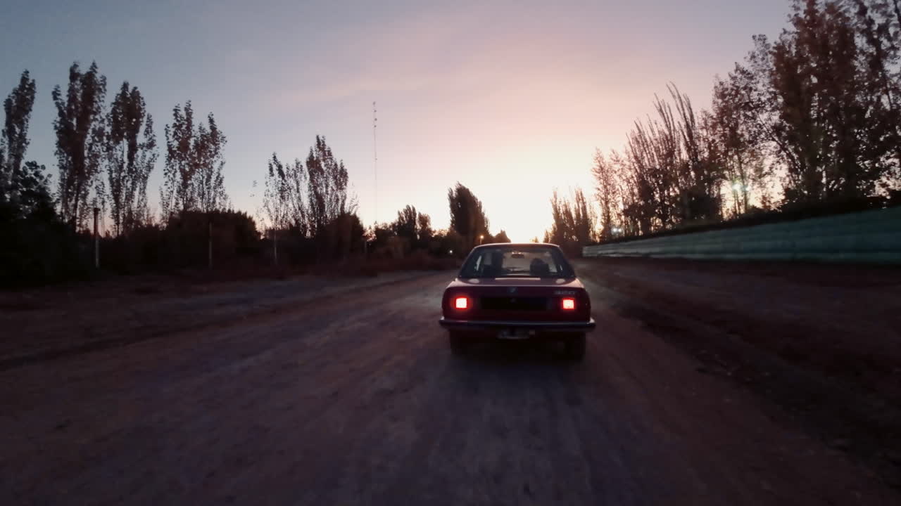 Red Car Driving on a Dirt Road at Sunset