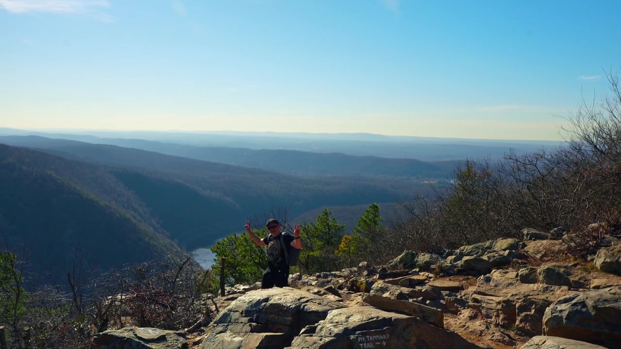 Escursionista con zaino in piedi su una cima rocciosa che si affaccia sul fiume. Vista laterale di un escursionista uomo che riposa sul bordo di una scogliera rocciosa. Vista panoramica della valle del fiume e delle montagne sullo sfondo.