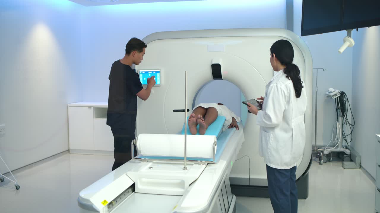 Personale che sistema il cuscino in gommapiuma blu dopo la regolazione della console TC, controlla il tablet e prepara il paziente per la scansione