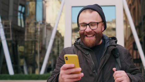 happy bearded man laughing while using smartphone in the city