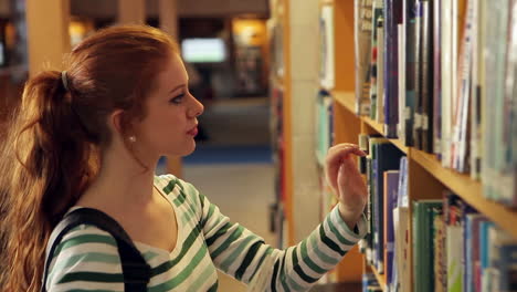 estudiante enfocado recogiendo un libro en la biblioteca