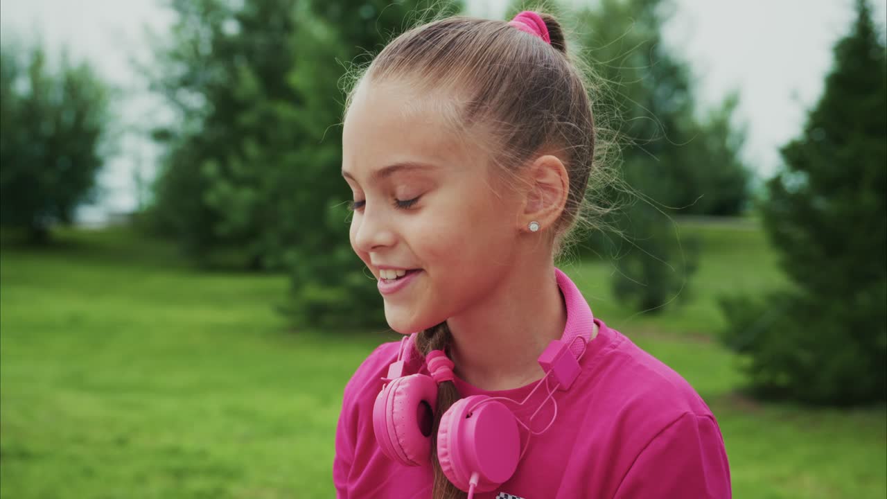 Uma jovem desfruta de seu tempo ao ar livre enquanto usa um dispositivo móvel, usando fones de ouvido rosa e uma roupa combinando, capturando alegria e inocência na natureza.