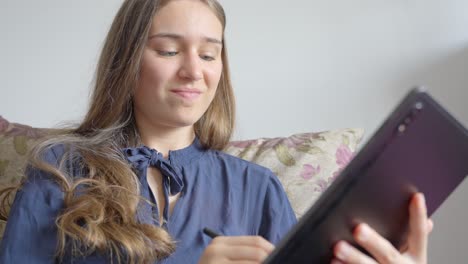 chica adolescente de ojos azules sonriendo mientras usa la tableta en el sofá