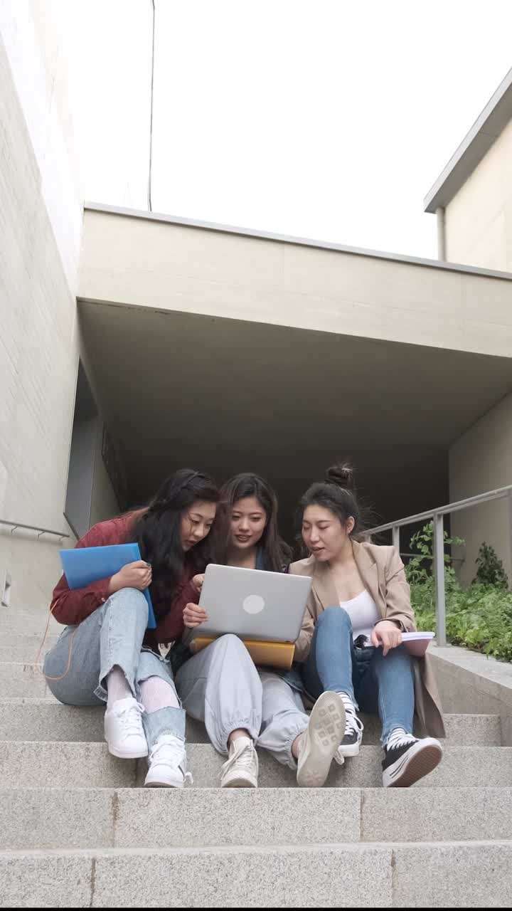 Gruppo di studentesse asiatiche che usano un laptop e studiano insieme sedute sulle scale del campus universitario