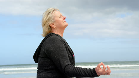 Side-view-of-old-caucasian-woman-meditating-at-beach-4k