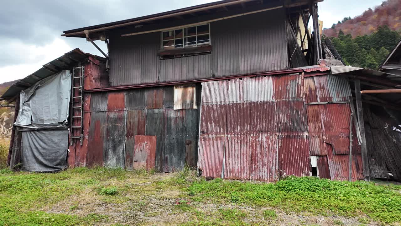 Dilapidated and patched building with corrugated iron walls and roof, showing signs of decay and disrepair in the rural landscape of Shirakawa go Village