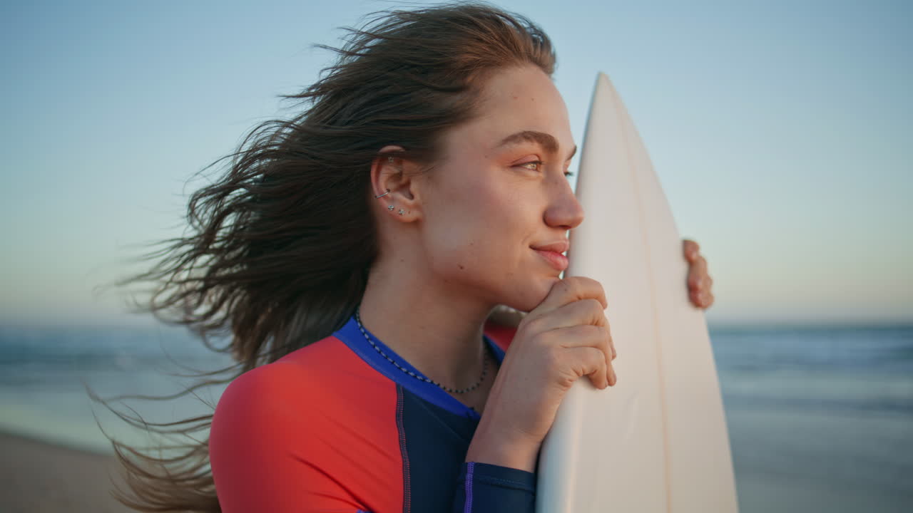 Dreamy model holding surfboard looking ocean waves at sunrise morning portrait